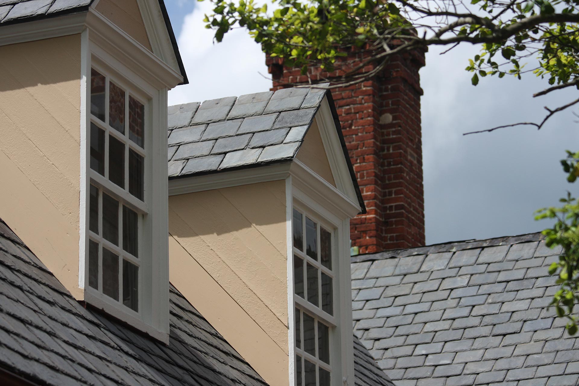 Traditional slate roof showcasing two dormer windows and a brick chimney on a classic residence